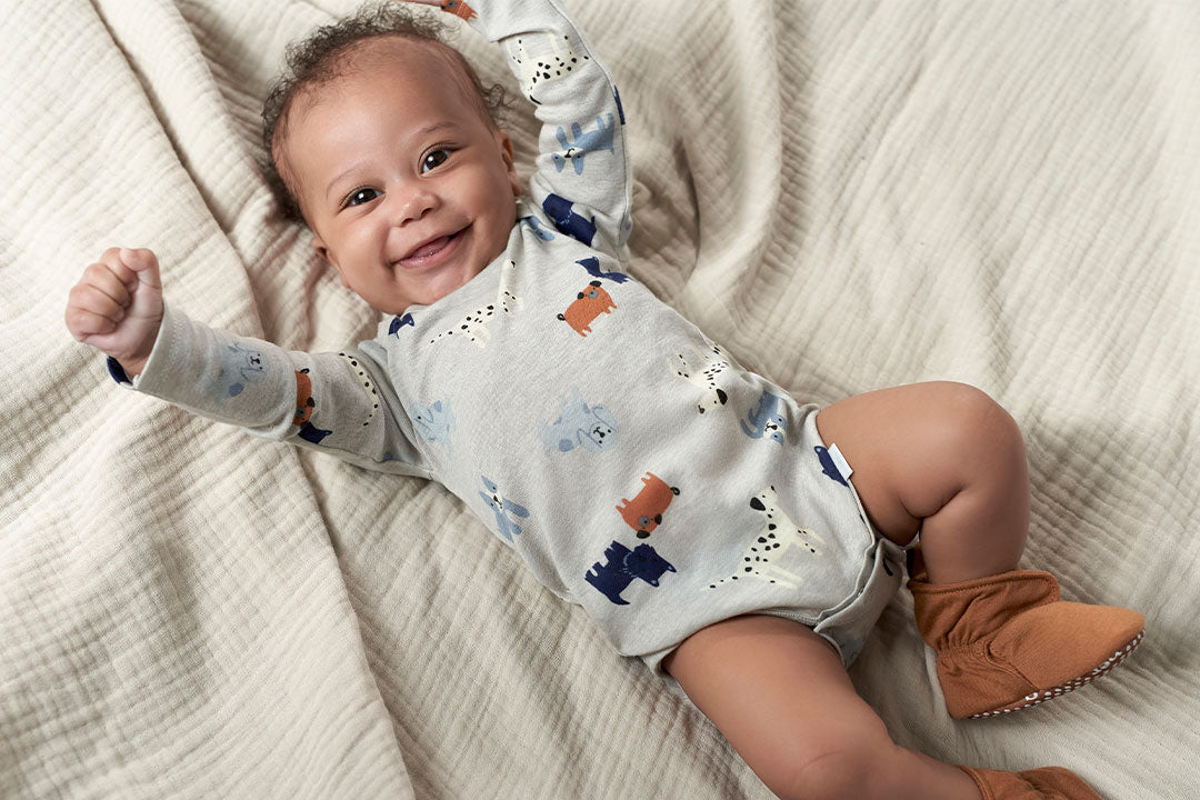 A delightful baby boy, dressed in a winter outfit, flashing a big smile while lying on a bed.