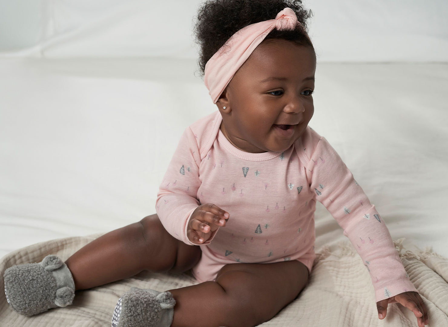 Snuggled up in a pink bodysuit, a sweet baby girl enjoys the cozy comfort of a bed during the winter season.