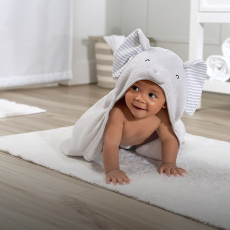 adorable baby crawling on floor in an elephant motif towel having fun after bathtime.